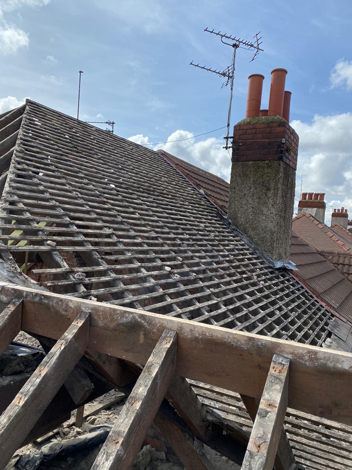A roof stripped back to the battens beside the chimney