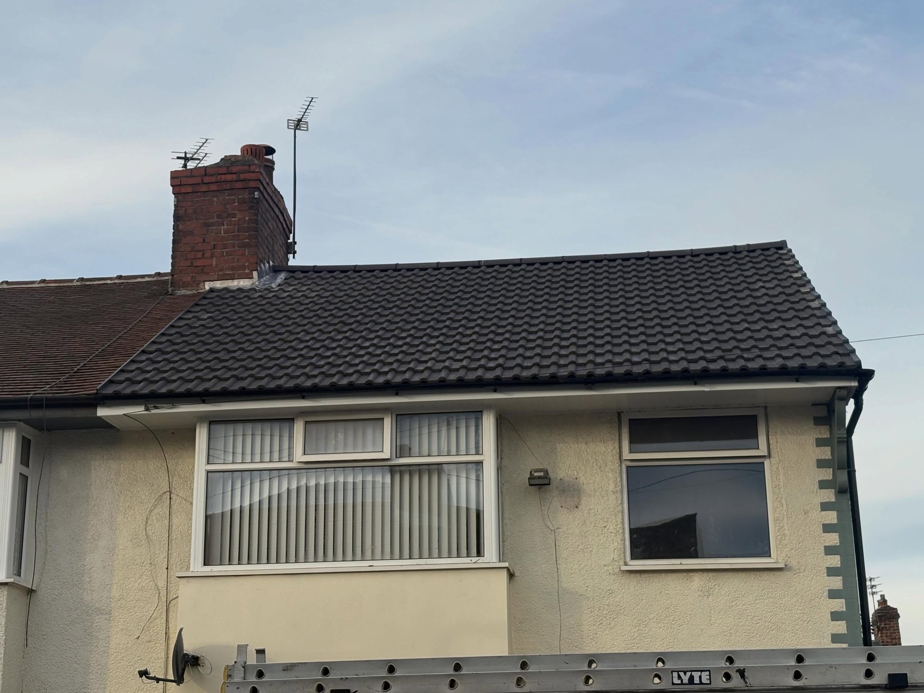 A finished dark tiled roof on a rendered bungalow, with the chimney above it