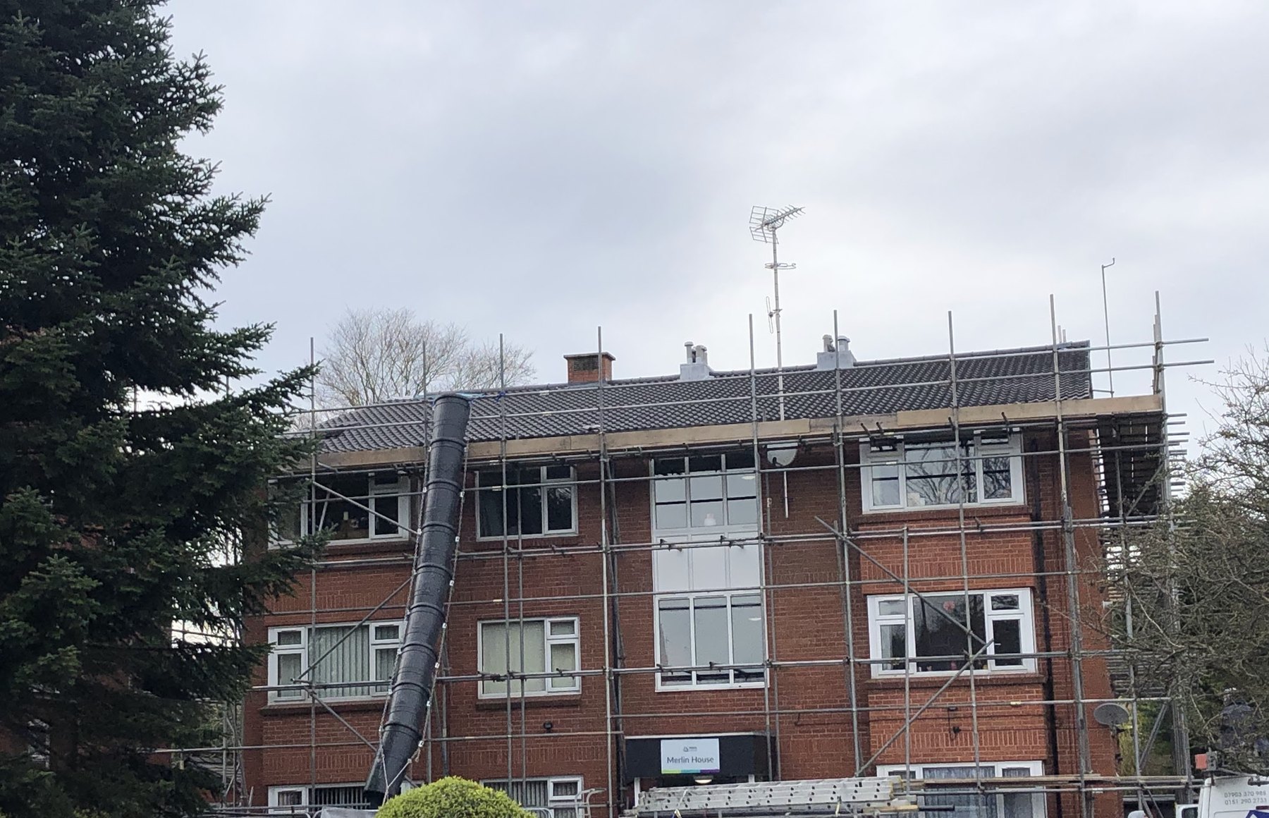 A three-storey block of flats scaffolded to the eaves, with a rubble chute down the front