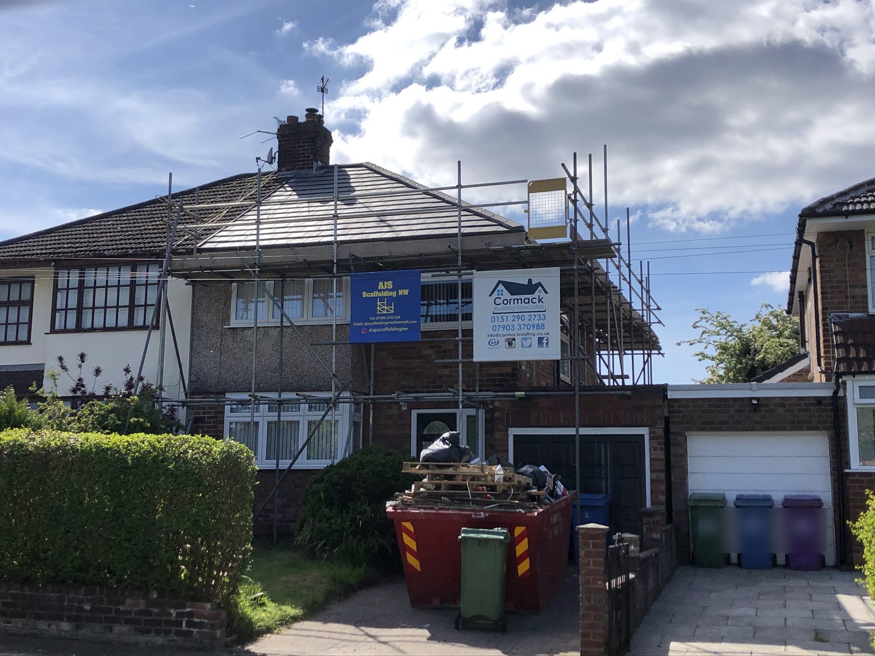 A semi-detached house mid re-roof, scaffold up and the Cormack Roofing board on the front